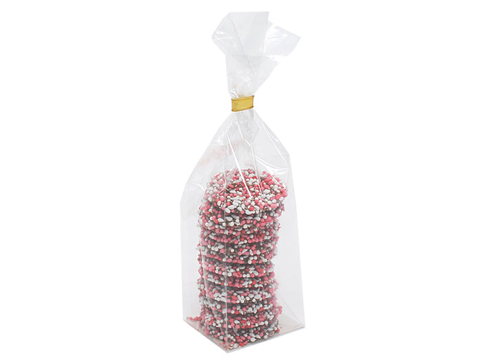 Høj, smal klar pose fyldt med en stak runde chokolader med lyserødt og hvidt drys, lukket foroven med et guldbånd